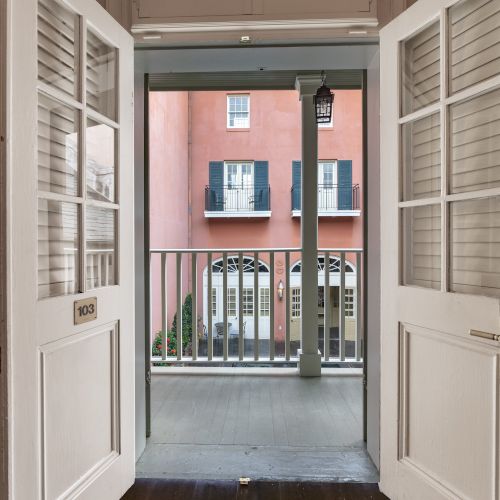 Looking through open double doors at a balcony railing, with a building visible across a courtyard.
