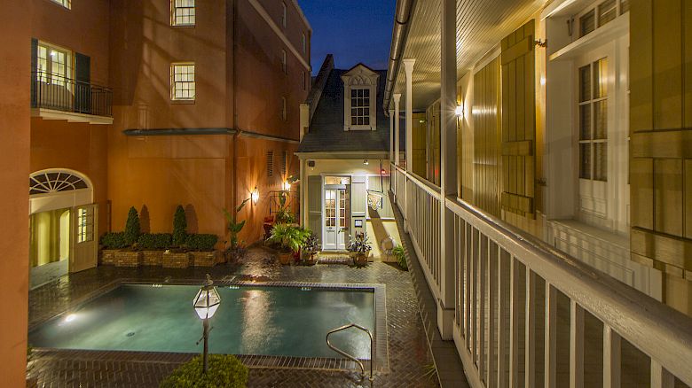A nighttime courtyard view with a lit swimming pool, surrounded by buildings featuring windows and balconies, and exterior lighting.