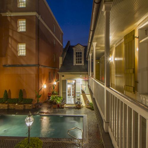 The image shows a cozy courtyard with a small pool, surrounded by buildings and lit by outdoor wall sconces and lamp posts.