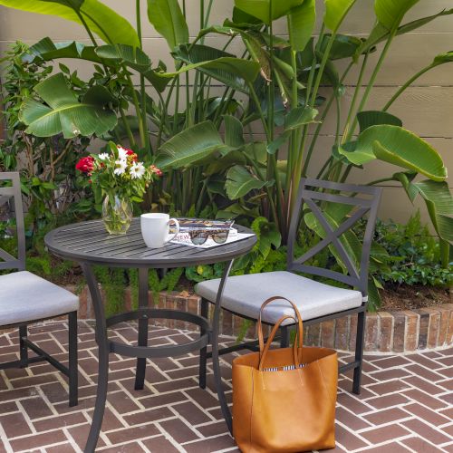 A patio set with two chairs and a table holding flowers, a mug, magazines, and sunglasses. A brown tote bag is on the floor.