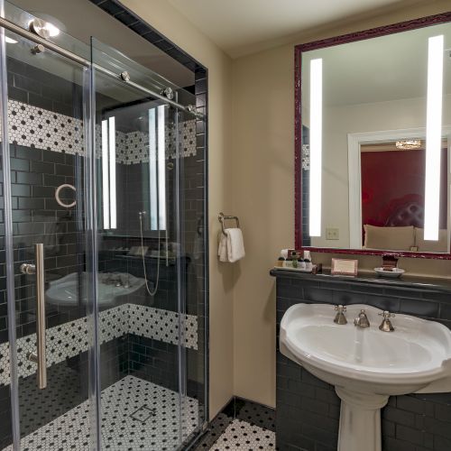 A modern bathroom with a glass shower, illuminated mirror, and sink with black and white tile accents.