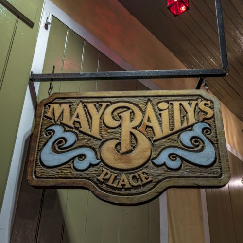 A rustic wooden sign reads "May Baily's Place," with decorative swirls, hangs below a red lantern.