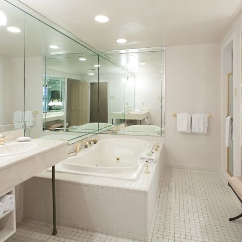 A spacious bathroom with a large mirrored wall, a bathtub, sink, towels, and elegant lighting fixtures, creating a luxurious feel.