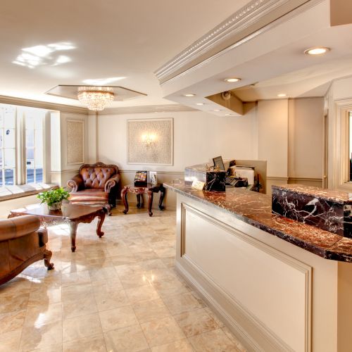 Luxurious reception area with marble counter, leather chairs, ornate tables, and elegant decor in warm, neutral tones.
