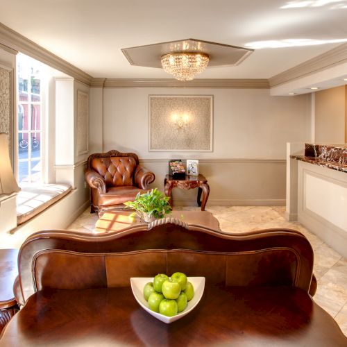 A cozy reception area with elegant décor, featuring leather chairs, a bowl of green apples, and a desk with guest services sign.