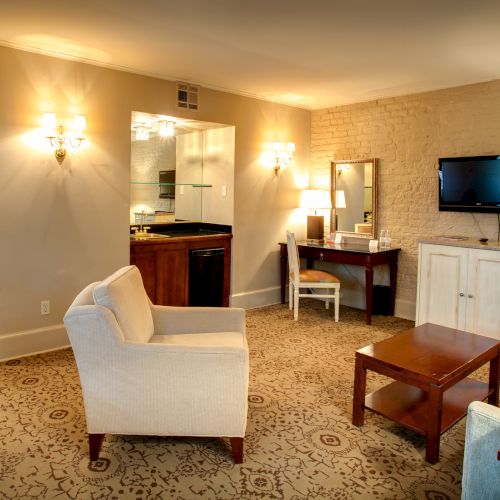 A cozy living room features a sofa, armchair, coffee table, wall-mounted TV, and a desk with chair and lamp.