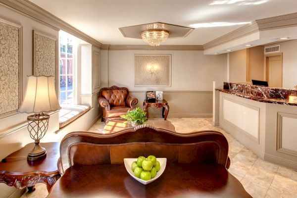 The image shows an elegant waiting area with leather chairs, a wooden table with green apples, decorative panels, and a reception desk.