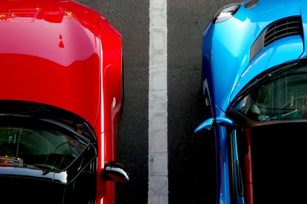 Top-down view of a red car and a blue car parked side by side, separated by a white line.